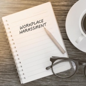 Workplace harassment concept on notebook with glasses, pencil and coffee cup on wooden table