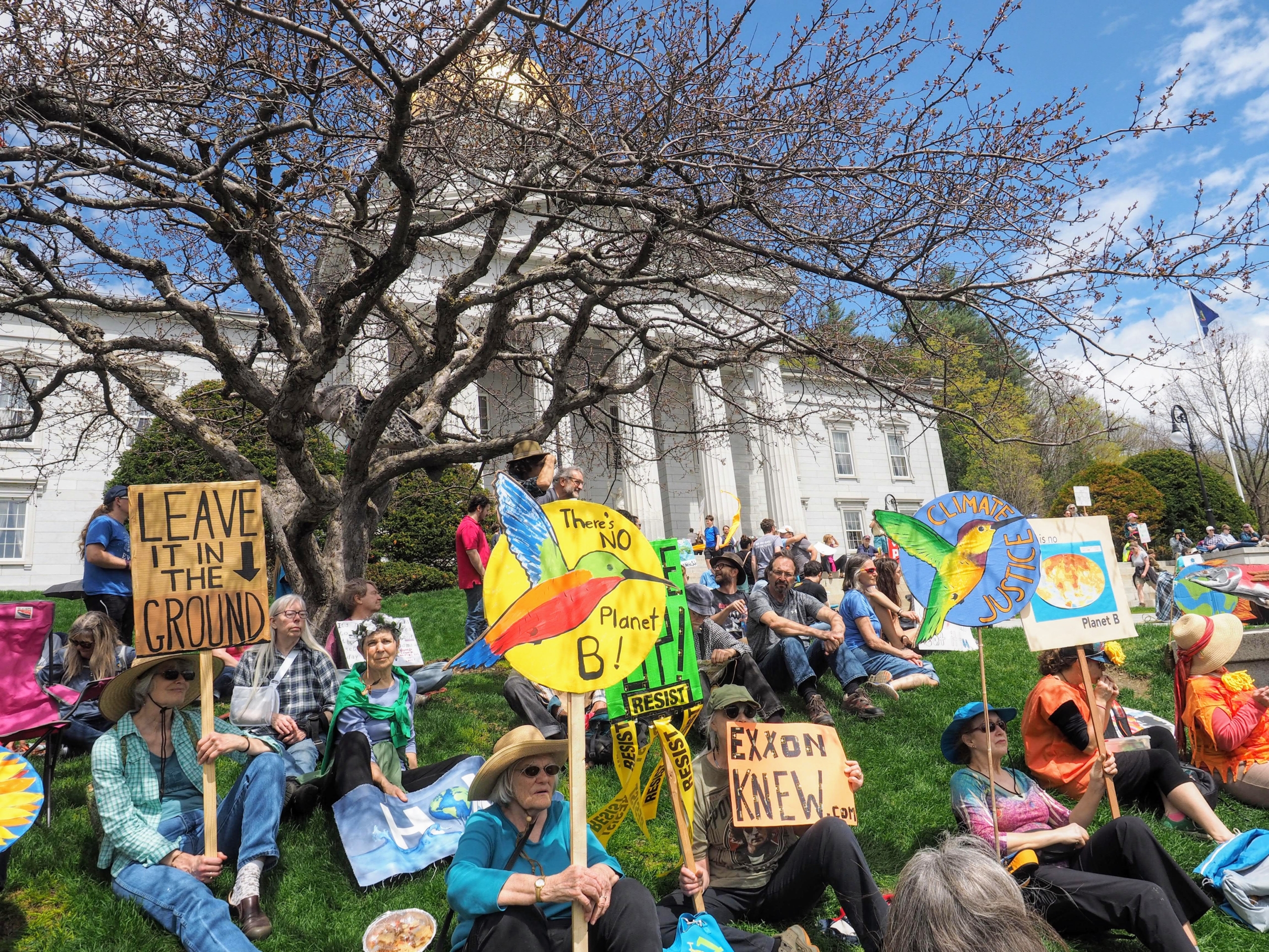 group of people outside a capital building with proteset signs about saving the environment